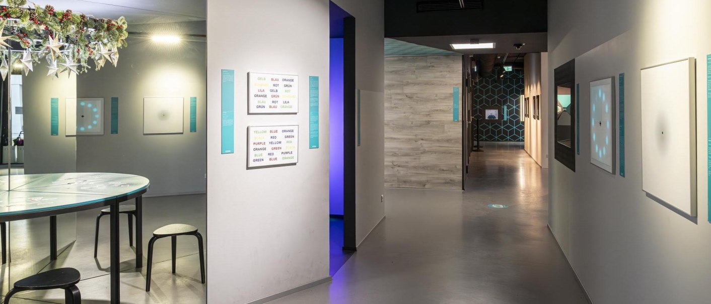 Innenansicht des Museums der Illusionen Stuttgart mit optischen Täuschungen an den Wänden und einem Tisch mit Hockern., © Stuttgart-Marketing GmbH, Sarah Schmid