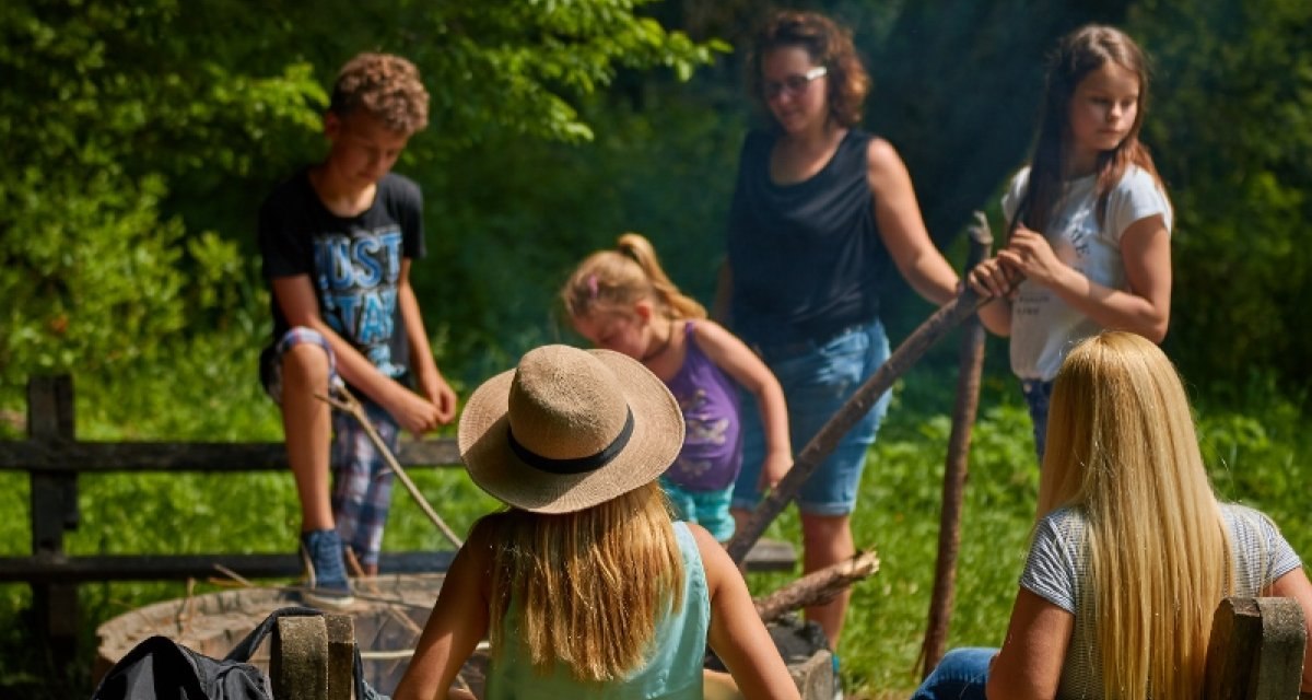 Eine Gruppe von Menschen sitzt und steht um einen Rastplatz im Wald. Sie scheinen sich zu unterhalten und die Natur zu genie&szlig;en., &copy; Natur.Nah. Sch&ouml;nbuch & Heckeng&auml;u