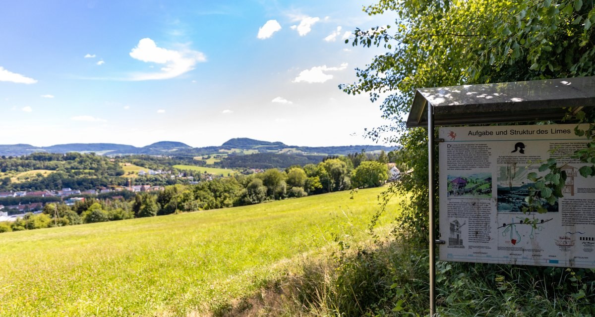 Grüne Wiesen und Hügel unter blauem Himmel. Rechts eine Infotafel über den Limes. Weitblick über die Landschaft., © Foto Thomas Zehnder Grüne Wiesen und Hügel unter blauem Himmel. Rechts eine Infotafel über den Limes. Weitblick über die Landschaft., © Foto Thomas Zehnder