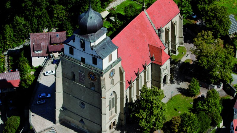 Luftaufnahme der Stiftskirche Herrenberg mit markantem Turm und rotem Dach, umgeben von Bäumen und Gebäuden., © Stuttgart-Marketing GmbH