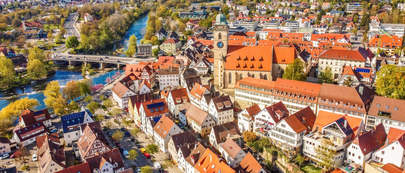 Luftaufnahme von Nürtingen im Frühling. Rote Dächer, eine Kirche und ein Fluss prägen das Stadtbild. Bäume blühen, die Landschaft ist grün., © Daniel Jüptner