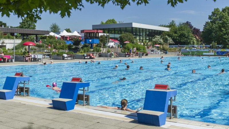 Ein Freibad mit vielen Schwimmern im Wasser. Im Hintergrund sind Liegestühle, Sonnenschirme und ein modernes Gebäude zu sehen., © Stadt Vaihingen an der Enz