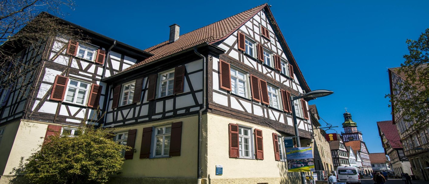 Seitliche Ansicht eines Fachwerkhauses in Kirchheim unter Teck, mit roten Fensterläden und blauem Himmel im Hintergrund., © SMG, Sarah Schmid Seitliche Ansicht eines Fachwerkhauses in Kirchheim unter Teck, mit roten Fensterläden und blauem Himmel im Hintergrund., © SMG, Sarah Schmid