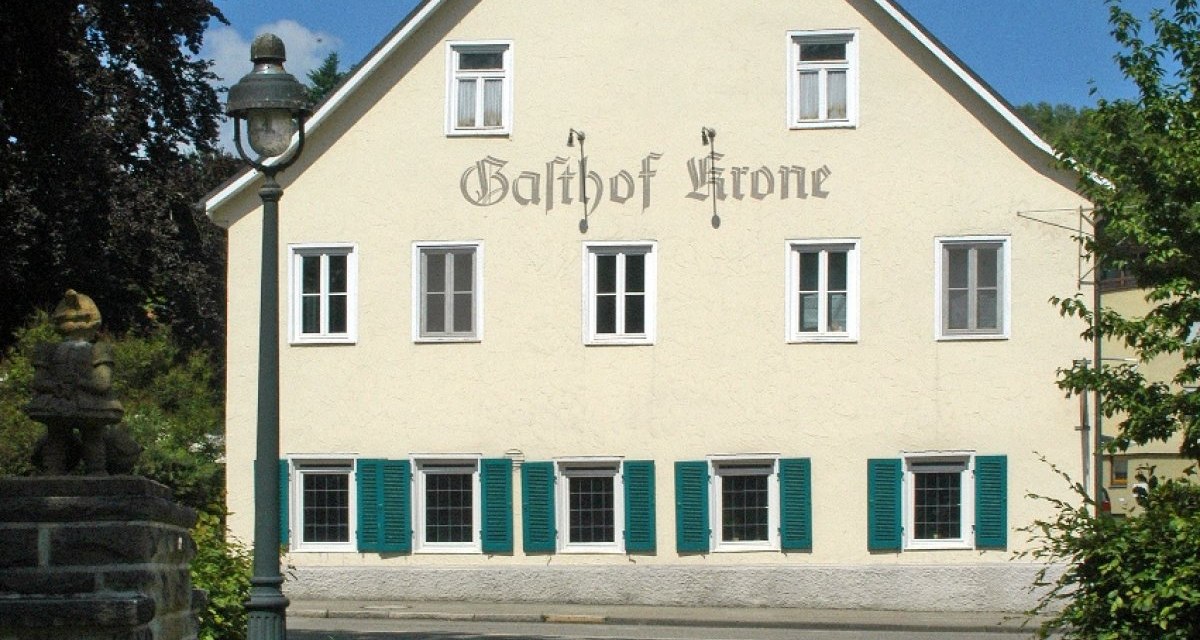 Traditionelles Geb&auml;ude mit der Aufschrift 'Gasthof Krone', gr&uuml;nen Fensterl&auml;den und einer Laterne im Vordergrund, bei sonnigem Wetter., &copy; Natur.Nah. Sch&ouml;nbuch & Heckeng&auml;u