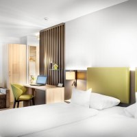 Modernes Hotelzimmer mit Doppelbett, grünem Kopfteil, Schreibtisch mit Laptop, Sofa und Kleiderschrank. Helle, freundliche Einrichtung., © TOMAS