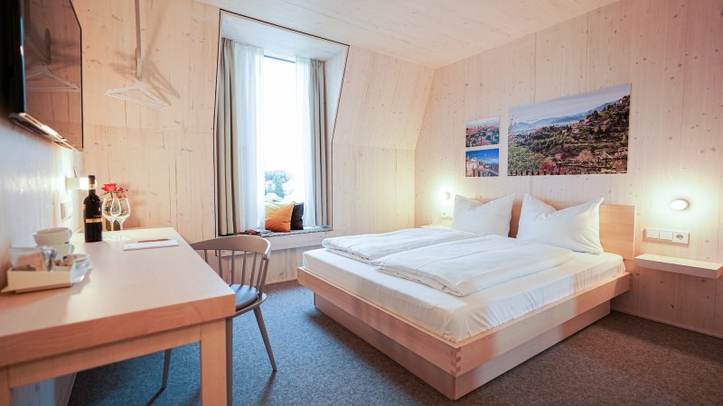 Modernes Hotelzimmer mit Holzwänden, Doppelbett, Schreibtisch und Fensterbank. An der Wand hängen Bilder von Landschaften., © Hotel Bergamo Modernes Hotelzimmer mit Holzwänden, Doppelbett, Schreibtisch und Fensterbank. An der Wand hängen Bilder von Landschaften., © Hotel Bergamo