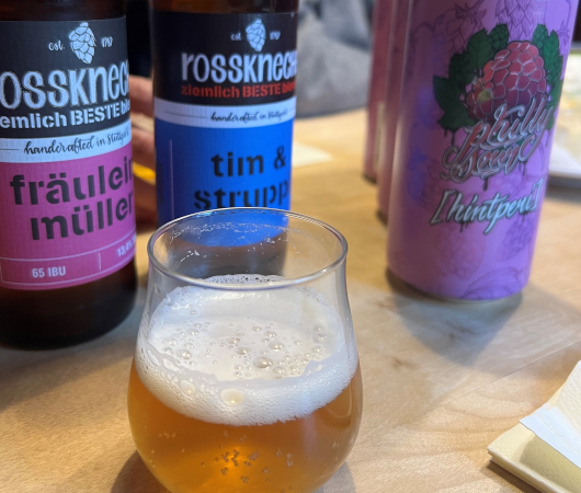 Verschiedene Bierflaschen und ein Glas Bier auf einem Tisch. Die Etiketten zeigen kreative Namen wie 'Fräulein Müller' und 'Tim & Struppi'., © Tourist Information und Ticket Service Ludwigsburg