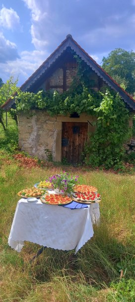 Ein Tisch mit Snacks steht auf einer Wiese vor einem alten Steinhaus, das mit Efeu bewachsen ist. Der Himmel ist bew&ouml;lkt., &copy; Renate Lohfink