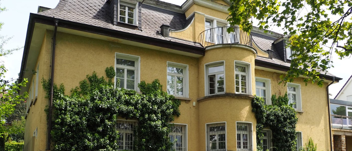 Eine gelbe Villa mit Efeu bewachsen, umgeben von einem gepflegten Garten. Die Architektur ist klassisch mit mehreren Fenstern und einem kleinen Balkon., &copy; Ruoff Stiftung