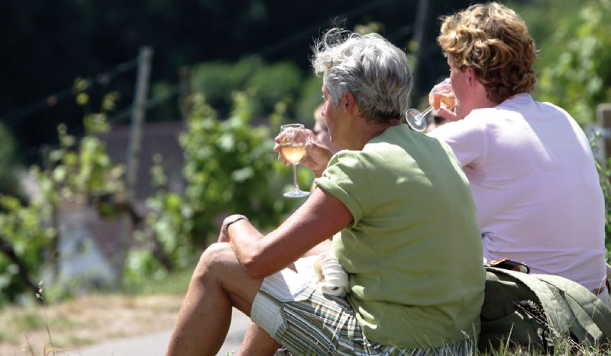 Zwei Personen sitzen im Gras und genießen ein Glas Wein auf einem Weinwanderweg. Im Hintergrund sind Weinreben zu sehen., © Stuttgart-Marketing GmbH Zwei Personen sitzen im Gras und genießen ein Glas Wein auf einem Weinwanderweg. Im Hintergrund sind Weinreben zu sehen., © Stuttgart-Marketing GmbH