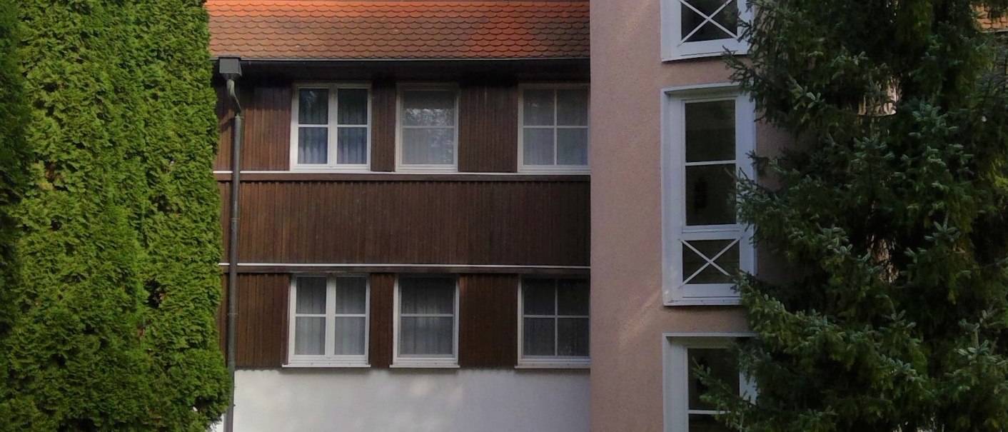 Ein mehrstöckiges Gebäude mit rundem Turm, Fenstern und rotem Dach, umgeben von Bäumen und grünem Rasen., © relexa Waldhotel Schatten Ein mehrstöckiges Gebäude mit rundem Turm, Fenstern und rotem Dach, umgeben von Bäumen und grünem Rasen., © relexa Waldhotel Schatten