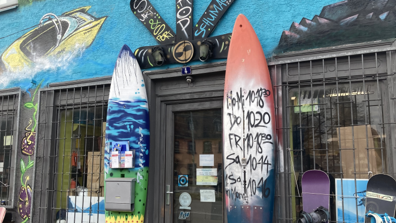 Surf- und Sportshop mit bunter Fassade, Surfbrettern und Snowboards vor dem Eingang. Graffiti und Wandmalereien schm&uuml;cken das Geb&auml;ude., &copy; L. Besmer