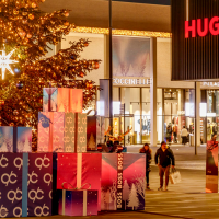 Weihnachtlich geschmückter Platz mit großem Baum und Geschenken vor dem Hugo Boss Geschäft. Menschen flanieren in der festlichen Atmosphäre., © OUTLETCITY AG