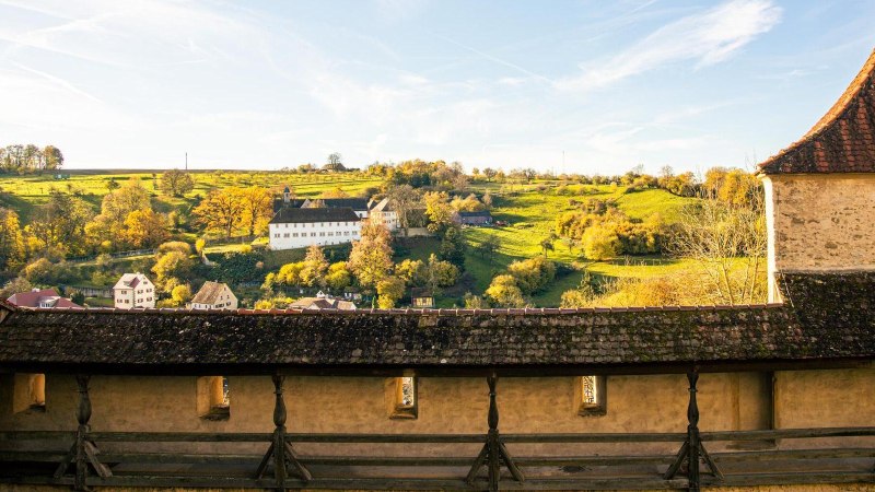 Blick von der Großcomburg auf eine malerische Landschaft mit einem weißen Gebäude und herbstlichen Bäumen im Hintergrund., © Stuttgart-Marketing GmbH, Sarah Schmid Blick von der Großcomburg auf eine malerische Landschaft mit einem weißen Gebäude und herbstlichen Bäumen im Hintergrund., © Stuttgart-Marketing GmbH, Sarah Schmid