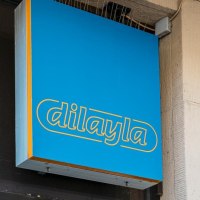 Blaues Schild mit gelber Aufschrift 'dilayla' an einer Gebäudewand, daneben ein grüner Pfeil., © Stuttgart Marketing GmbH, Sarah Schmid Blaues Schild mit gelber Aufschrift 'dilayla' an einer Gebäudewand, daneben ein grüner Pfeil., © Stuttgart Marketing GmbH, Sarah Schmid