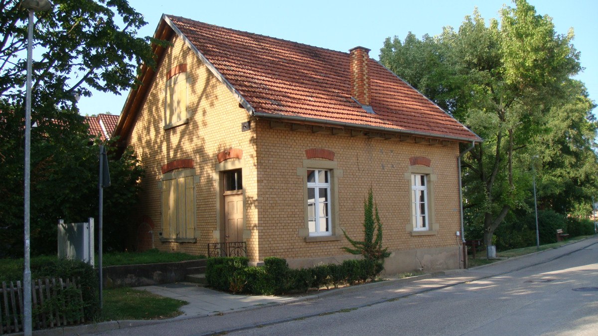 Ein kleines Backsteinhaus mit rotem Ziegeldach und Schornstein, umgeben von Bäumen und einer Straße., © Land der 1000 Hügel - Kraichgau-Stromberg