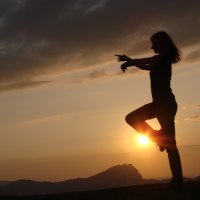 Silhouette einer Person in Balancepose vor einem malerischen Sonnenuntergang, mit Bergen im Hintergrund und dramatischen Wolken am Himmel., © Kurverwaltung Beuren