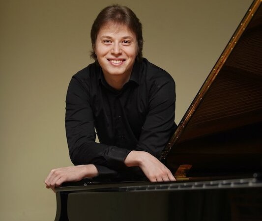 Eine Person in schwarzem Hemd lehnt sich lächelnd auf einen Flügel. Der Hintergrund ist schlicht und hell., © Stadt Böblingen - Amt für Kultur