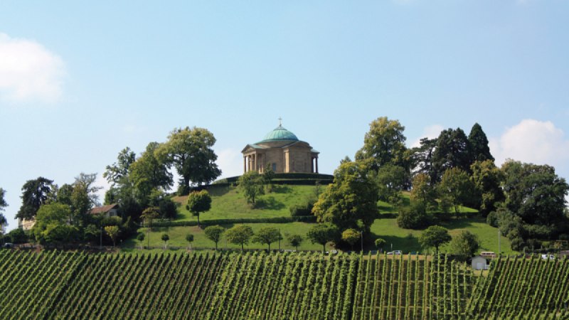 Die Grabkapelle auf dem Württemberg thront auf einem Hügel, umgeben von grünen Weinbergen und Bäumen unter einem blauen Himmel., © Stuttgart-Marketing GmbH Die Grabkapelle auf dem Württemberg thront auf einem Hügel, umgeben von grünen Weinbergen und Bäumen unter einem blauen Himmel., © Stuttgart-Marketing GmbH