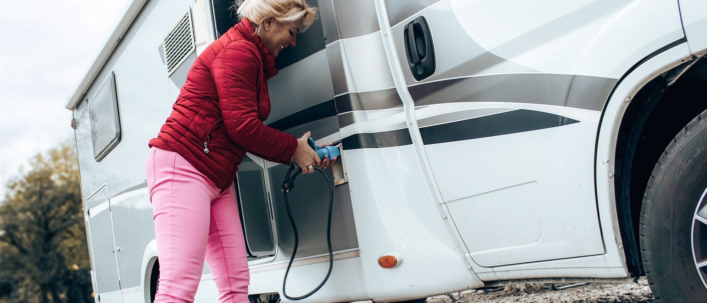 Eine Frau in roter Jacke und pinker Hose schließt ein Wohnmobil an eine Stromquelle an. Sie hält ein blaues Kabel in der Hand., © Erlebnisregion Schwäbischer Albtrauf e. V. Eine Frau in roter Jacke und pinker Hose schließt ein Wohnmobil an eine Stromquelle an. Sie hält ein blaues Kabel in der Hand., © Erlebnisregion Schwäbischer Albtrauf e. V.
