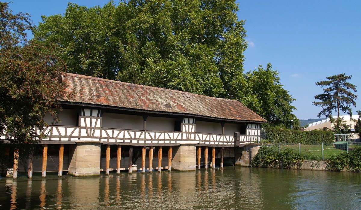 Fachwerkbrücke über den Neckar in Esslingen, umgeben von Bäumen und Wasser. Der Himmel ist klar und blau., © Thomas Krebs Fachwerkbrücke über den Neckar in Esslingen, umgeben von Bäumen und Wasser. Der Himmel ist klar und blau., © Thomas Krebs
