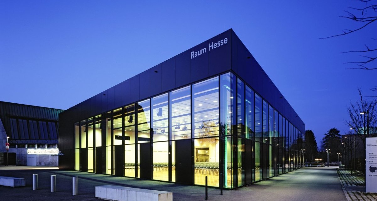 Die Schwabenlandhalle Fellbach bei Dämmerung. Moderne Glasfassade mit beleuchtetem Innenraum, umgeben von einem gepflasterten Weg und Bäumen., © Schwabenlandhalle Fellbach Die Schwabenlandhalle Fellbach bei Dämmerung. Moderne Glasfassade mit beleuchtetem Innenraum, umgeben von einem gepflasterten Weg und Bäumen., © Schwabenlandhalle Fellbach