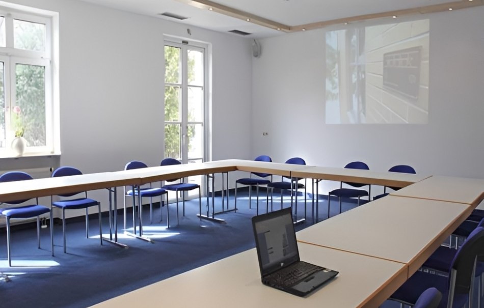Leerer Konferenzraum mit U-förmigen Tischen, blauen Stühlen und einem Laptop. Ein Projektor zeigt ein Bild an der Wand., © Hotel Neuwirtshaus Leerer Konferenzraum mit U-förmigen Tischen, blauen Stühlen und einem Laptop. Ein Projektor zeigt ein Bild an der Wand., © Hotel Neuwirtshaus