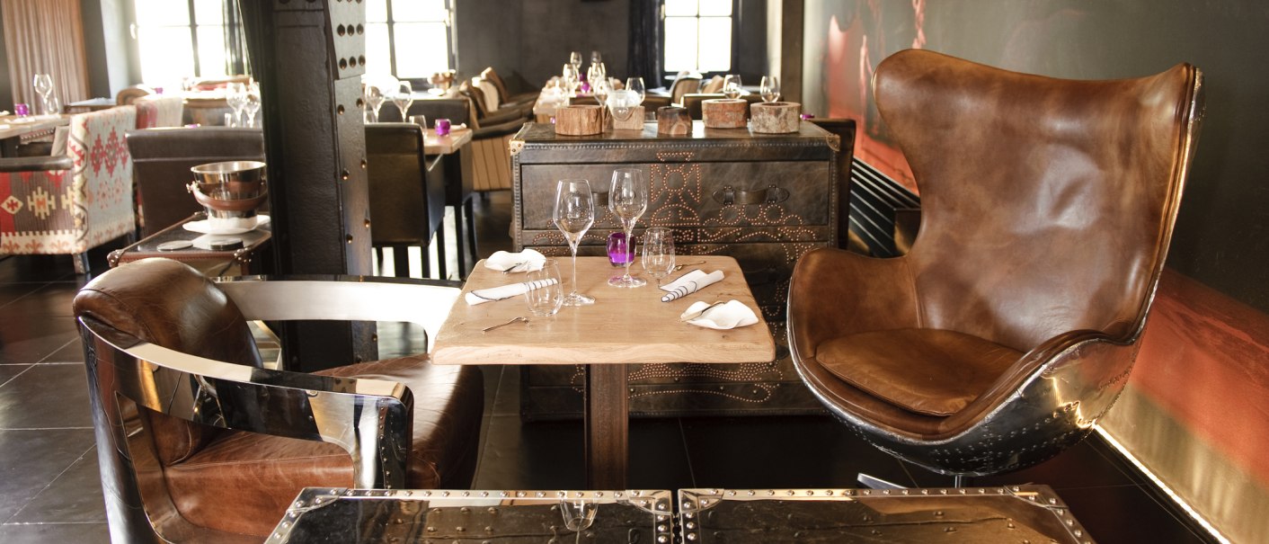 Ein stilvoll eingerichtetes Restaurant mit Ledersesseln und einem gedeckten Tisch. Im Hintergrund sind weitere Tische und Stühle zu sehen., © none