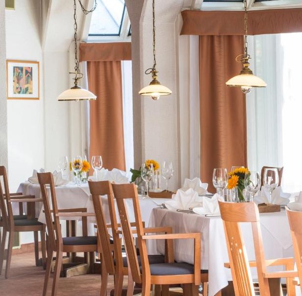 Ein elegantes Restaurant mit gedeckten Tischen, Holzst&uuml;hlen und Sonnenblumen als Dekoration. Gro&szlig;e Fenster lassen viel Licht herein., &copy; cSchupfnudl