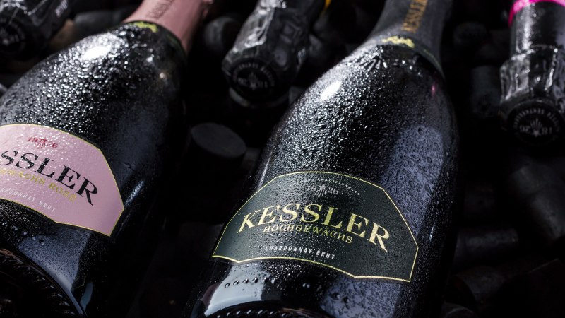 Nahaufnahme von Kessler Sektflaschen, die mit Wassertropfen bedeckt sind. Die Etiketten zeigen verschiedene Sorten wie Rosé und Chardonnay Brut., © none Nahaufnahme von Kessler Sektflaschen, die mit Wassertropfen bedeckt sind. Die Etiketten zeigen verschiedene Sorten wie Rosé und Chardonnay Brut., © none