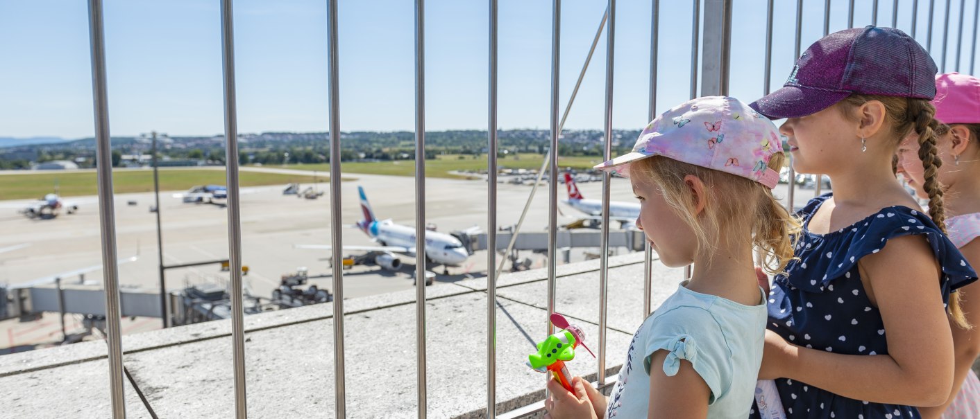 Kinder stehen auf der Besucherterrasse des Stuttgarter Flughafens und schauen durch ein Gitter auf das Rollfeld mit Flugzeugen., © Flughafen Stuttgart