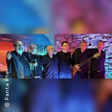 Eine Band steht vor einer farbig beleuchteten Steinwand und posiert f&uuml;r ein Foto. Die Mitglieder tragen dunkle Kleidung., &copy; links im Bild