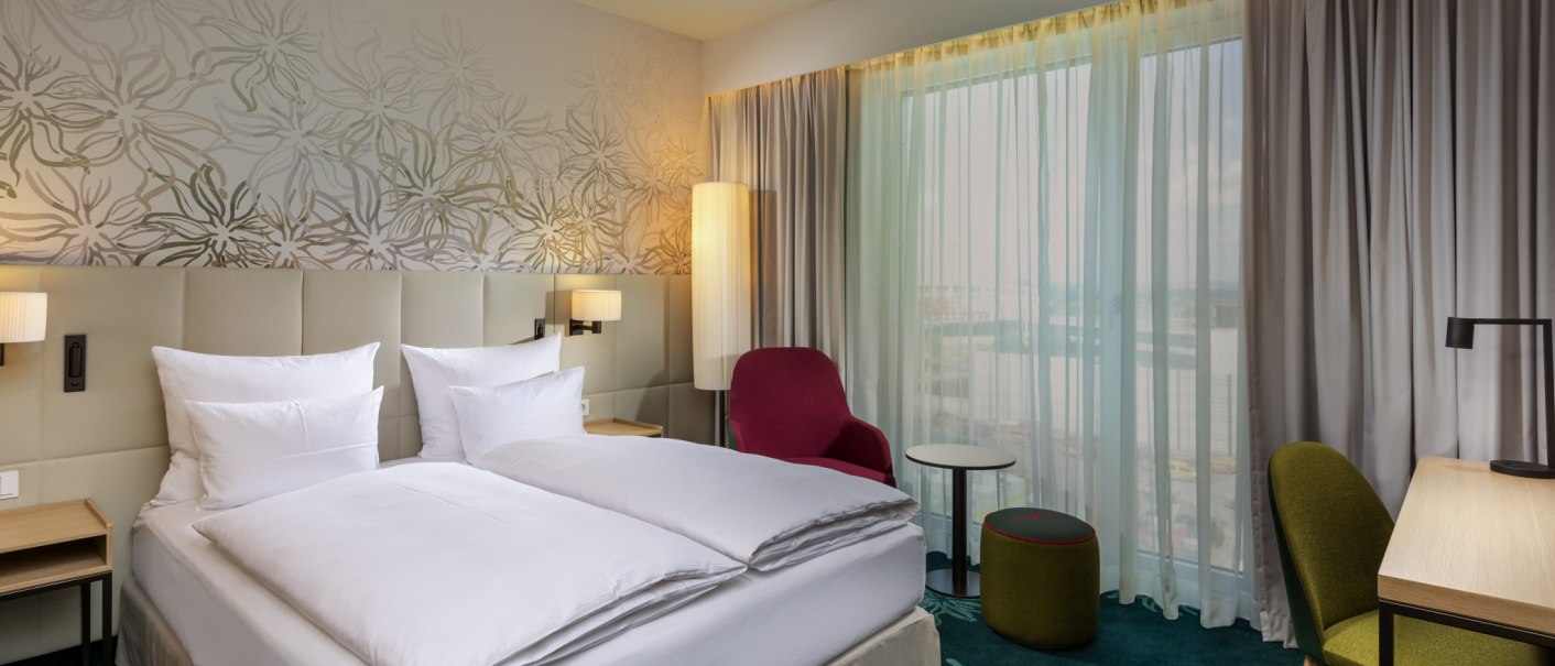 Modernes Hotelzimmer mit Doppelbett, rotem Sessel, grünem Stuhl und Schreibtisch. Große Fenster mit Vorhängen und floraler Wandgestaltung., © Mövenpick Hotel Stuttgart Messe & Congress Modernes Hotelzimmer mit Doppelbett, rotem Sessel, grünem Stuhl und Schreibtisch. Große Fenster mit Vorhängen und floraler Wandgestaltung., © Mövenpick Hotel Stuttgart Messe & Congress