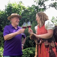 Ein Mann und eine Frau sto&szlig;en im Garten mit Rotweingl&auml;sern an. Die Frau tr&auml;gt ein traditionelles Kost&uuml;m und einen Wanderstock., &copy; Foto: G&uuml;nther Schuster
