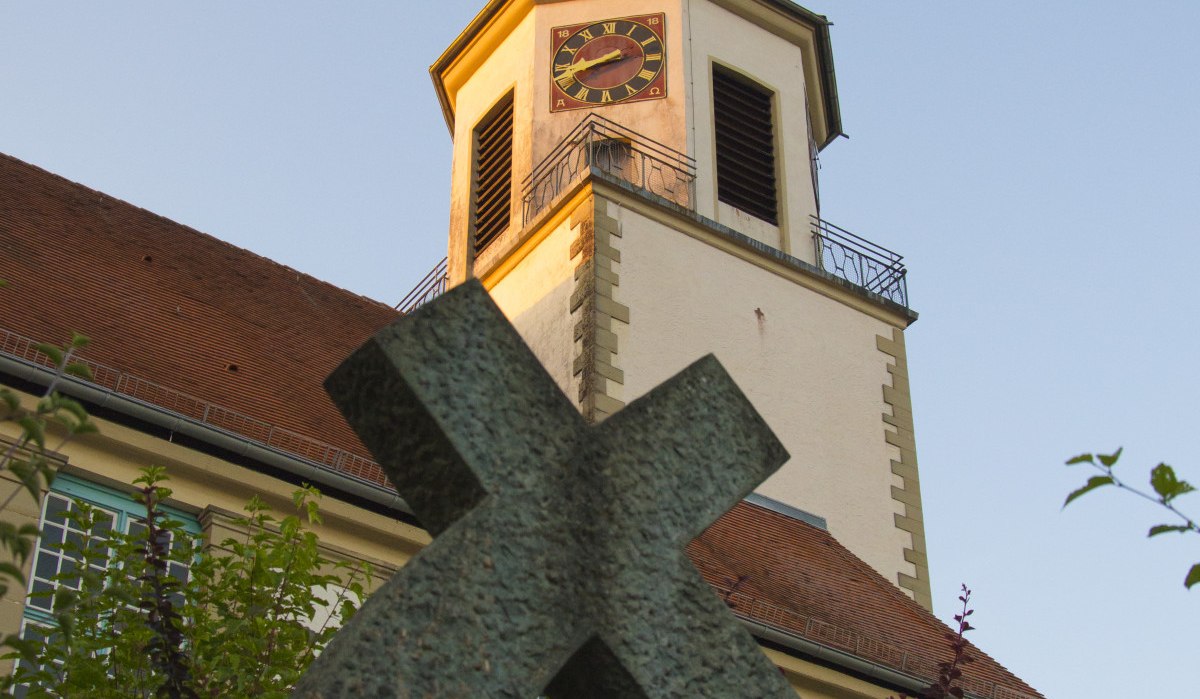 Kirchturm mit Uhr und Wetterhahn, im Vordergrund ein schräges Kreuz, umgeben von Pflanzen., © Unbekannt Kirchturm mit Uhr und Wetterhahn, im Vordergrund ein schräges Kreuz, umgeben von Pflanzen., © Unbekannt
