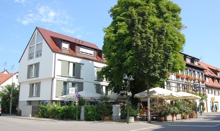 Moderne und traditionelle Geb&auml;ude an einer Stra&szlig;enecke, mit einem gro&szlig;en Baum und einem Caf&eacute; mit Sonnenschirmen., &copy; Jeanette Bender