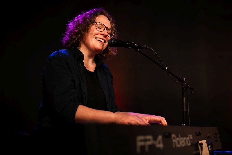 Eine Person mit Brille spielt lächelnd Keyboard und singt in ein Mikrofon auf einer Bühne., © Kulturhaus Schwanen Eine Person mit Brille spielt lächelnd Keyboard und singt in ein Mikrofon auf einer Bühne., © Kulturhaus Schwanen