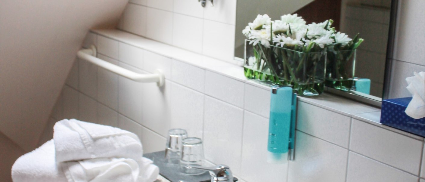 Ein Badezimmer mit Waschbecken, weißen Handtüchern, einem Spiegel, Blumen und einem Dachfenster., © Hotel Princess