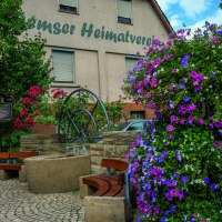 Blumenreicher Platz mit Brunnen und B&auml;nken vor einem Geb&auml;ude des Heimatvereins in Remseck am Neckar.