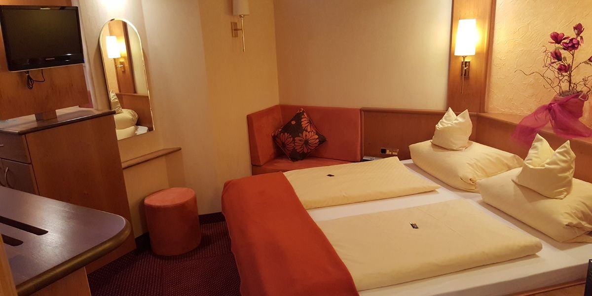 Gemütliches Doppelzimmer mit großem Bett, Fernseher, Spiegel und dekorativen Elementen. Warme Farben und einladende Atmosphäre., © Hotel Koch Gemütliches Doppelzimmer mit großem Bett, Fernseher, Spiegel und dekorativen Elementen. Warme Farben und einladende Atmosphäre., © Hotel Koch