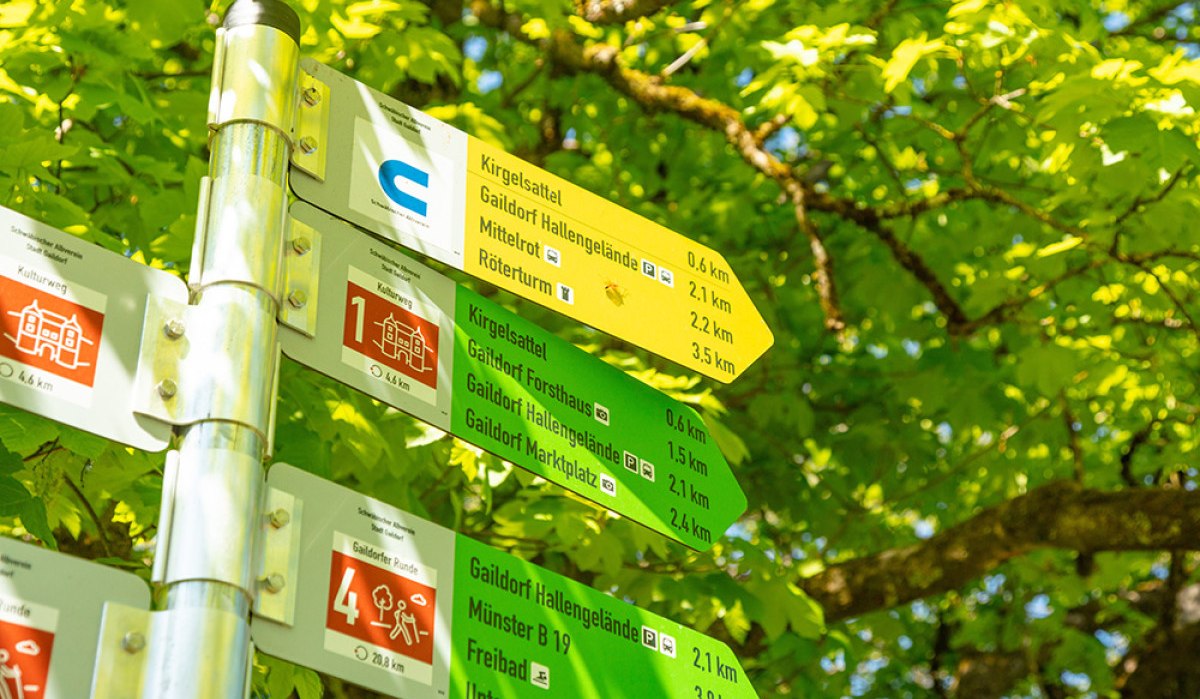 Wegweiser für Rundwanderwege in Gaildorf mit Entfernungsangaben, umgeben von grünem Laub. Wegweiser für Rundwanderwege in Gaildorf mit Entfernungsangaben, umgeben von grünem Laub.