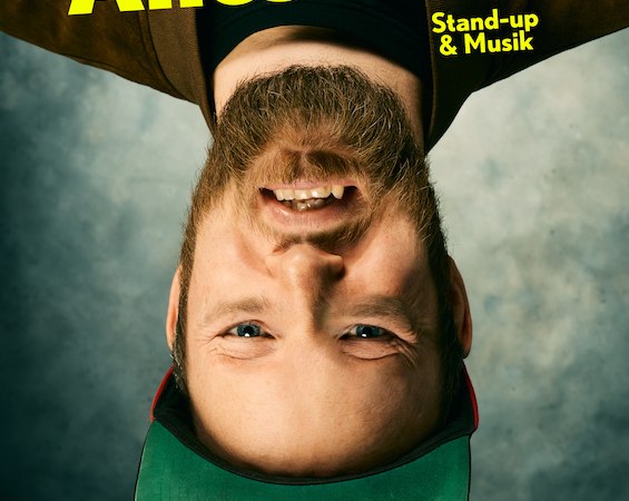 Ein Mann mit Bart und grüner Kappe steht auf dem Kopf. Text: 'Quichotte Alles echt. Stand-up & Musik'., © Scala Kultur Live gGmbH