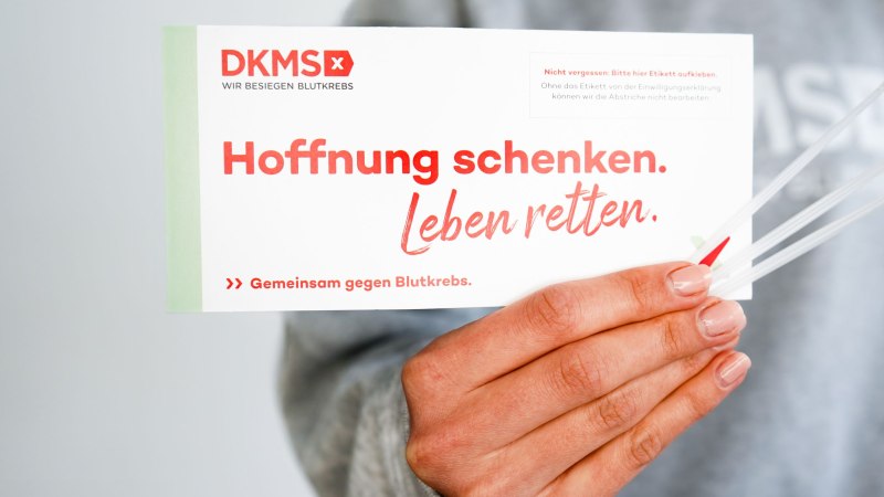 Hand, die ein DKMS-Registrierungsset hält - drei Wattestäbchen und einen Umschlag mit der Aufschrift "Hoffnung schenken. Leben retten.", © DKMS