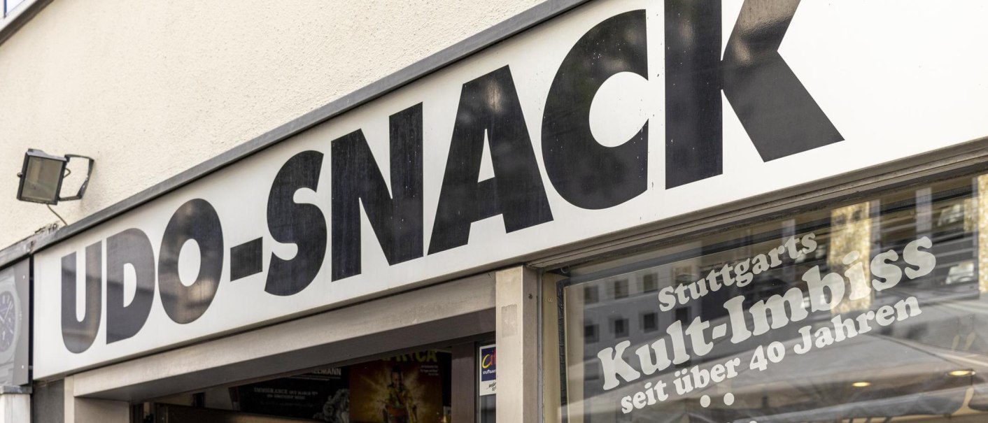 Schild mit der Aufschrift 'UDO-SNACK', darunter 'Stuttgarts Kult-Imbiss seit über 40 Jahren'. Außenansicht eines Imbissladens., © SMG, Sarah Schmid
