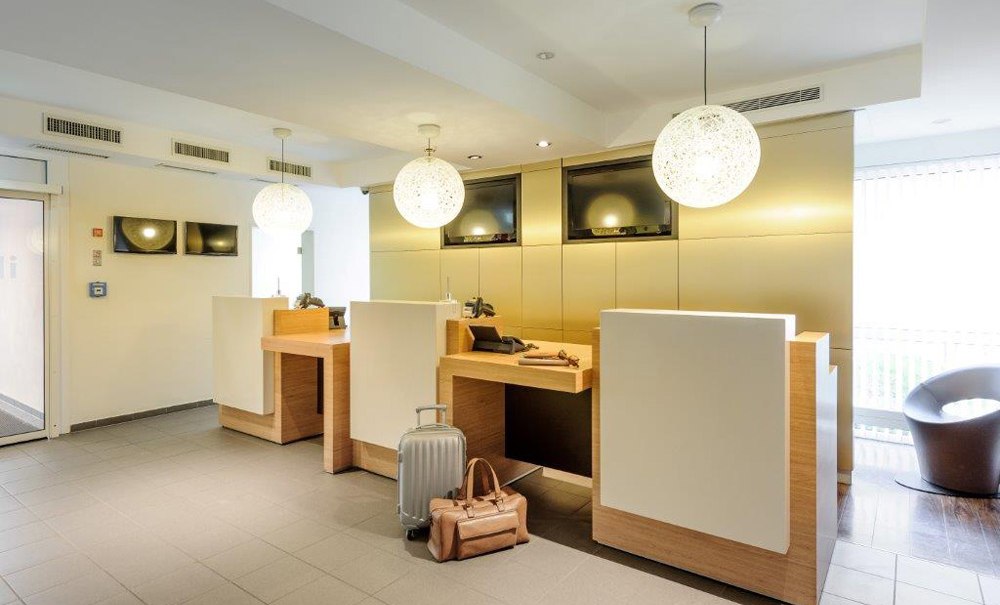 Moderne Hotelrezeption mit drei Schaltern, zwei Koffern im Vordergrund und stilvollen Lampen., © Ibis Stuttgart Airport Messe Moderne Hotelrezeption mit drei Schaltern, zwei Koffern im Vordergrund und stilvollen Lampen., © Ibis Stuttgart Airport Messe