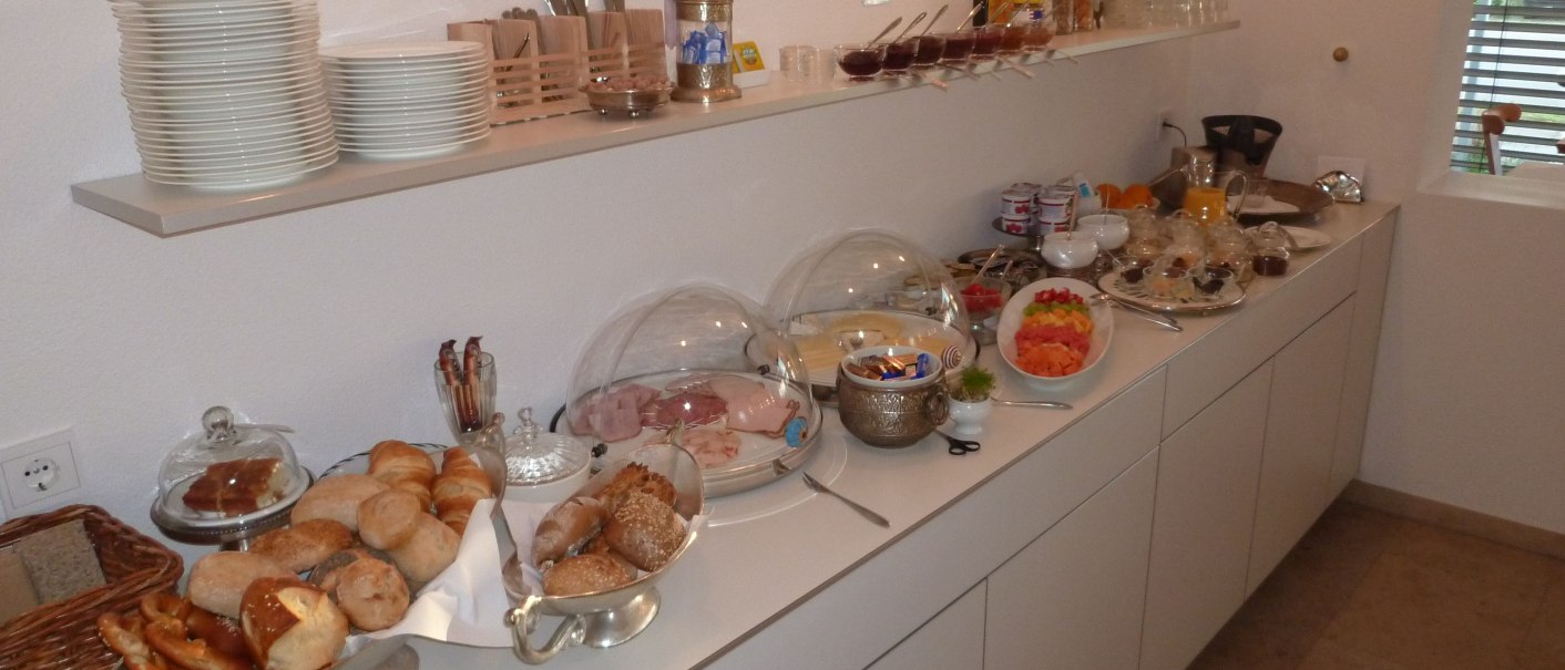 Ein Frühstücksbuffet mit Brötchen, Aufschnitt, Obst und Getränken auf einer weißen Theke in einem Hotel., © hotelmärchen GmbH