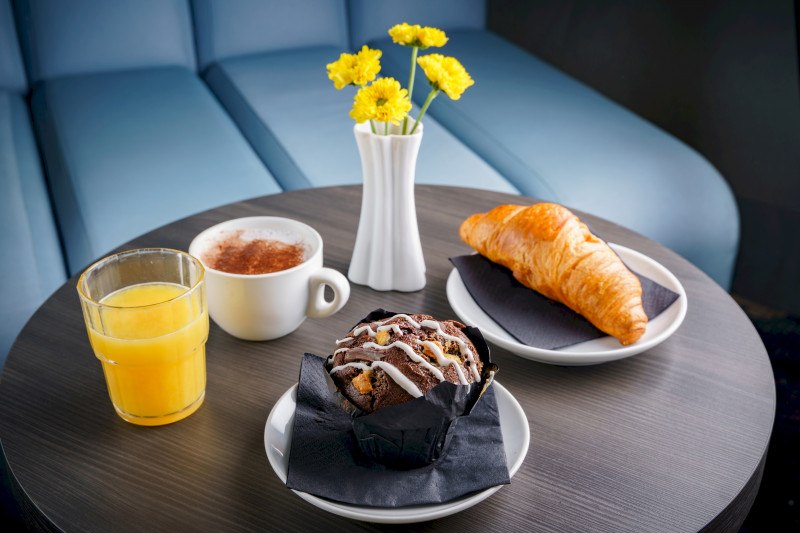 Ein Tisch mit Croissant, Schokomuffin, Orangensaft, Cappuccino und gelben Blumen in einer Vase., © A&O Hostels Marketing GmbH