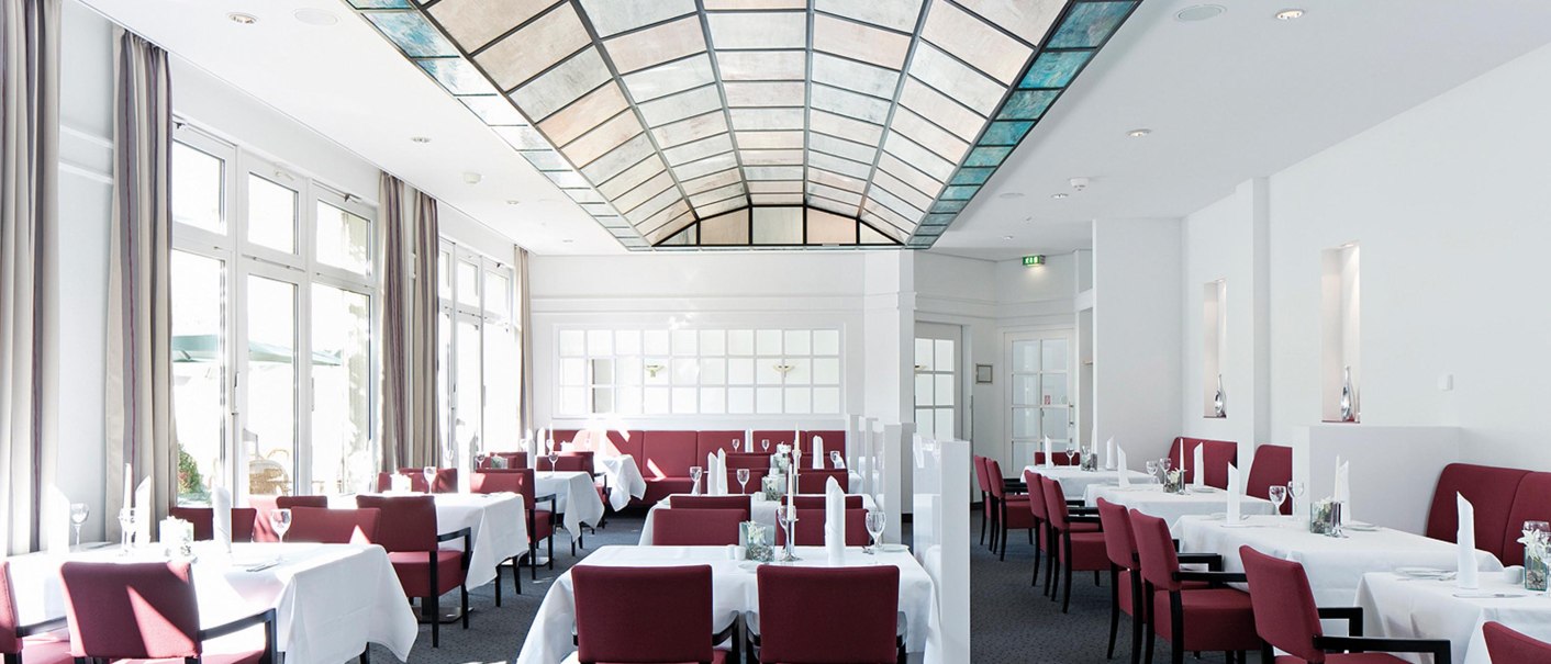 Elegantes Restaurant mit roten Stühlen, weißen Tischdecken und einem Glasdach. Helle Fensterfront und stilvolle Einrichtung., © Seminaris Hotel Bad Boll Elegantes Restaurant mit roten Stühlen, weißen Tischdecken und einem Glasdach. Helle Fensterfront und stilvolle Einrichtung., © Seminaris Hotel Bad Boll