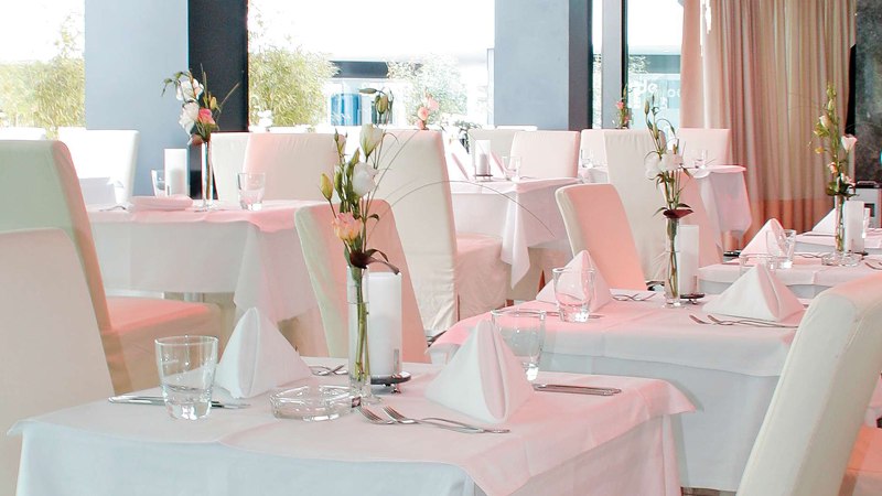 Elegantes Restaurant mit wei&szlig;en Tischdecken, stilvoll gedeckten Tischen und Blumenarrangements. Helle, moderne Einrichtung mit gro&szlig;en Fenstern., &copy; AMICI
