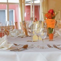 Eleganter Tisch im Hotel-Restaurant mit wei&szlig;en Servietten, Gl&auml;sern und Kerzen. Blumendekoration in Orange. Gro&szlig;e Fenster im Hintergrund., &copy; Hotel-Restaurant "Talblick"
